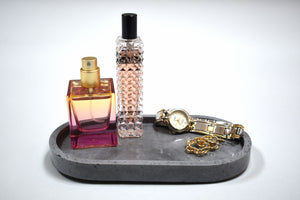 Gray Oval Concrete Tray  with 2 pink bottles of perfume, a watch, and a pair of earringson White Marble Background