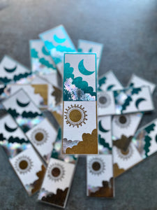 1 blue moon and gold sun bookmark in focus with a pile of other moon and sun bookmarks in the background