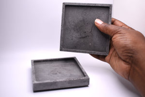 picture of hand holding a gray square coaster on a white background